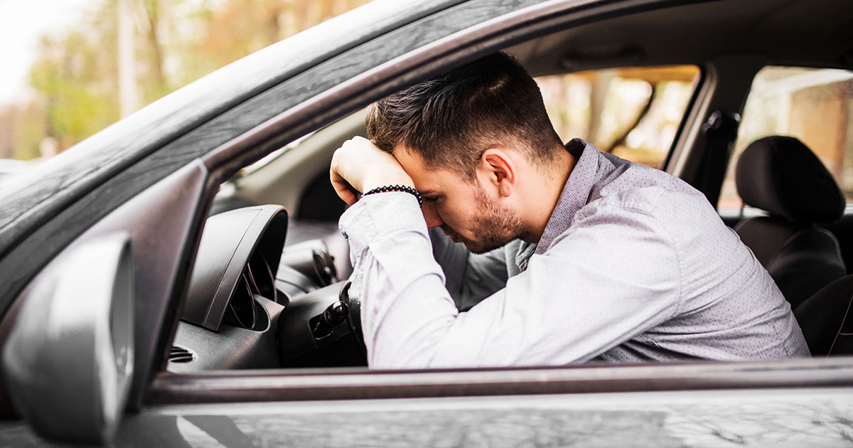 Fiatal férfi stresszesen ül az autóban vezetés előtt